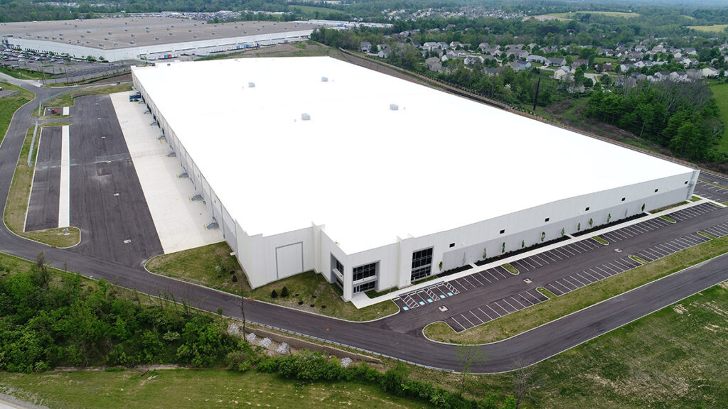 Large white industrial warehouse with TPO roof and empty parking lot.