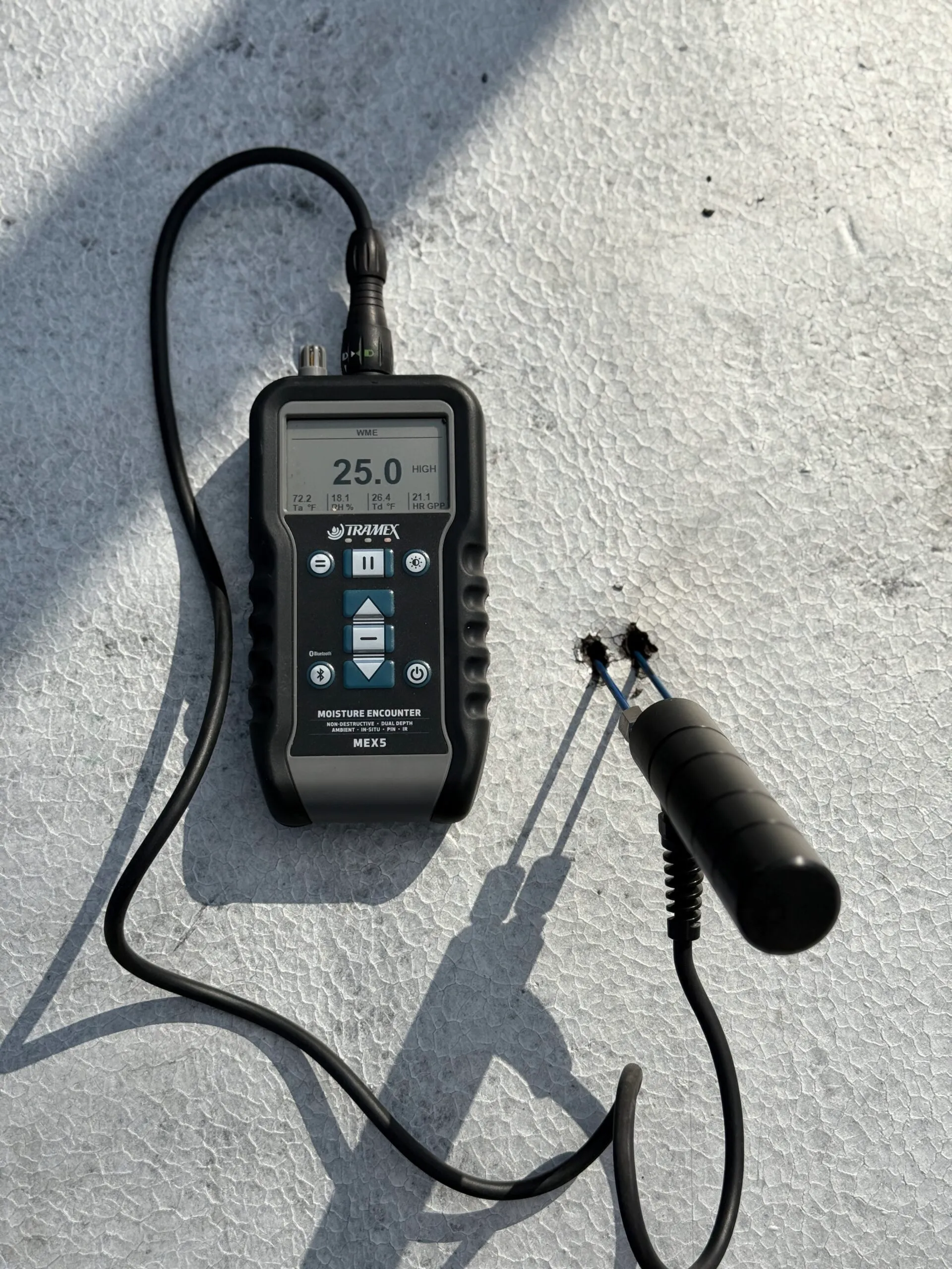Digital moisture meter reading roof surface moisture in bright daylight.