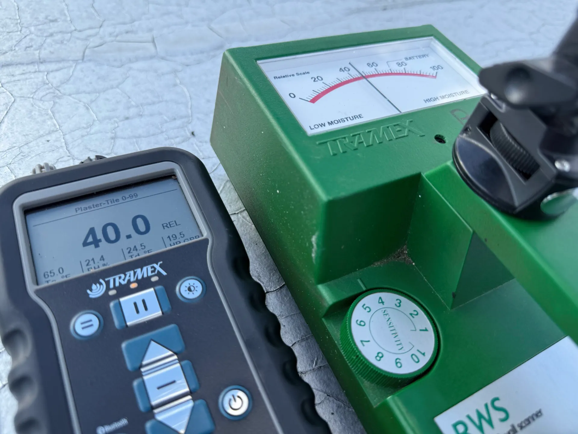 Tramex and digital moisture meters placed on gravel rooftop for inspection.